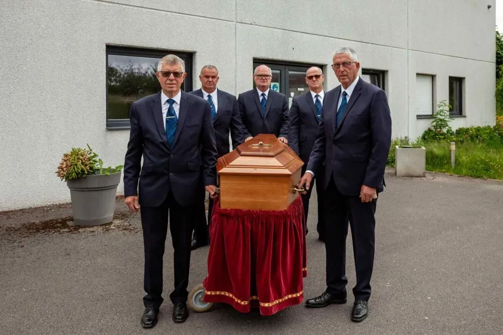 Porteurs funéraires entourant un cercueil placé sur un chariot